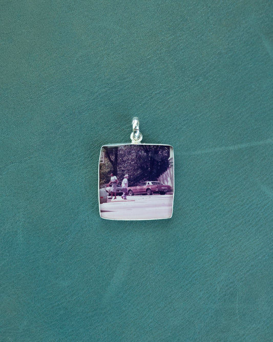 Silver pendant with a photo of two people walking on a street, against a teal background