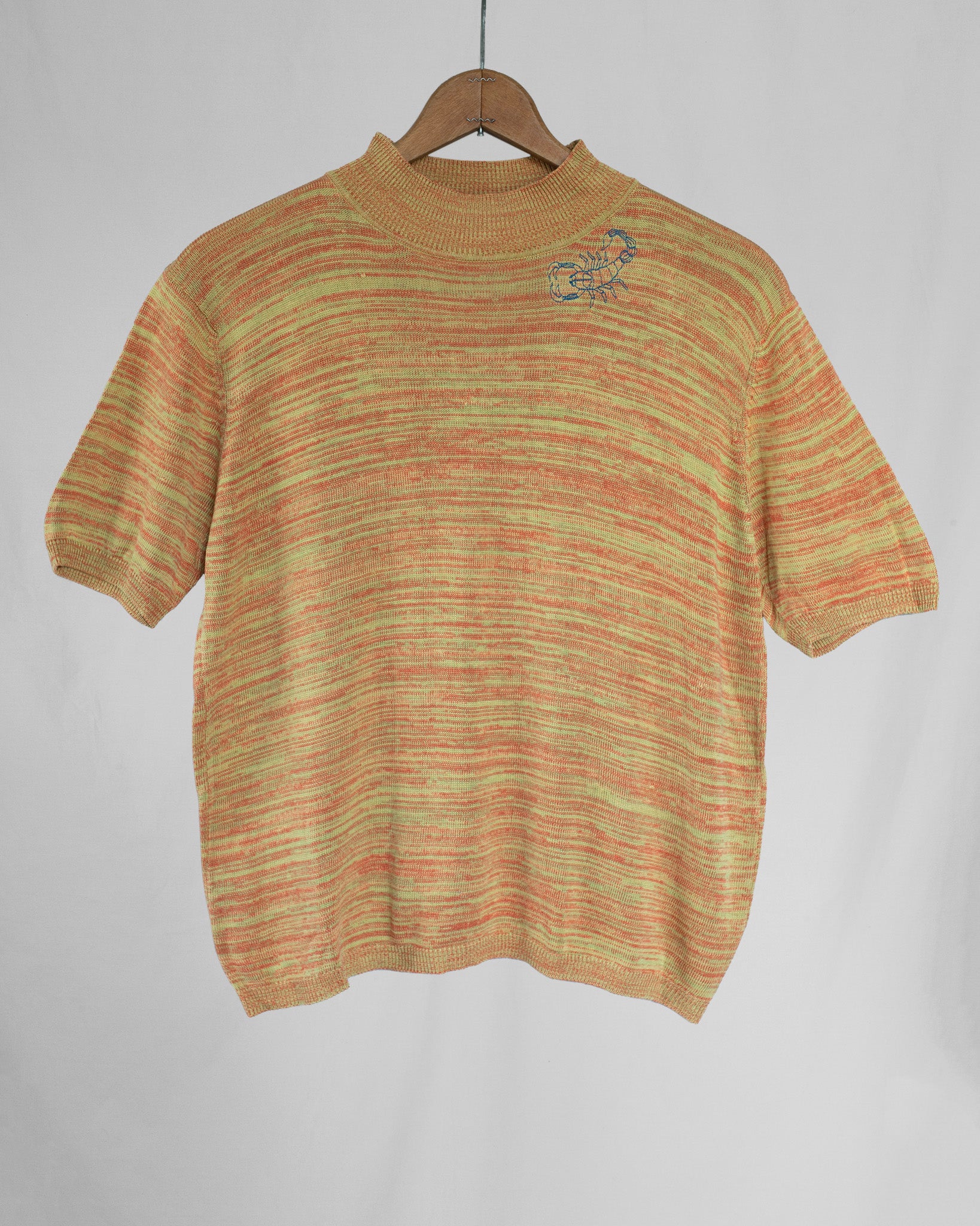 Knitted sweater with a scorpion embroidery on a hanger against a plain background.