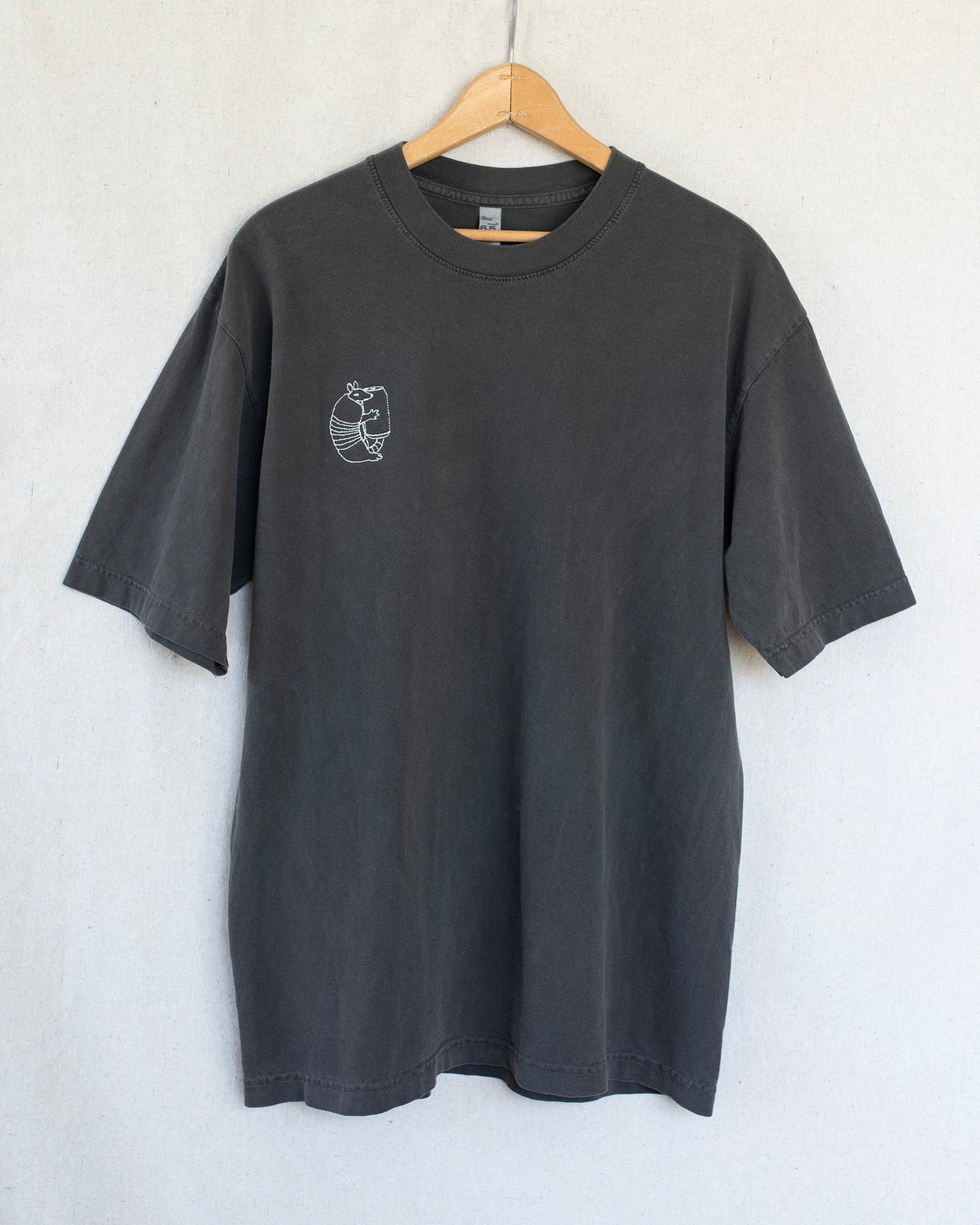 Black t-shirt with a small embroidery on a hanger against a light gray background