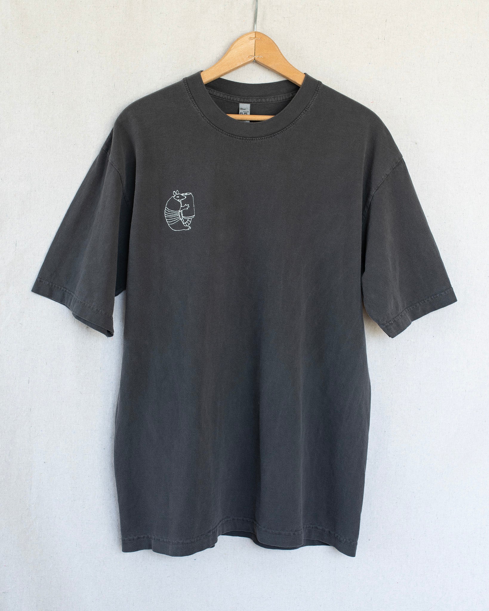 Black t-shirt with a small embroidery on a hanger against a light gray background