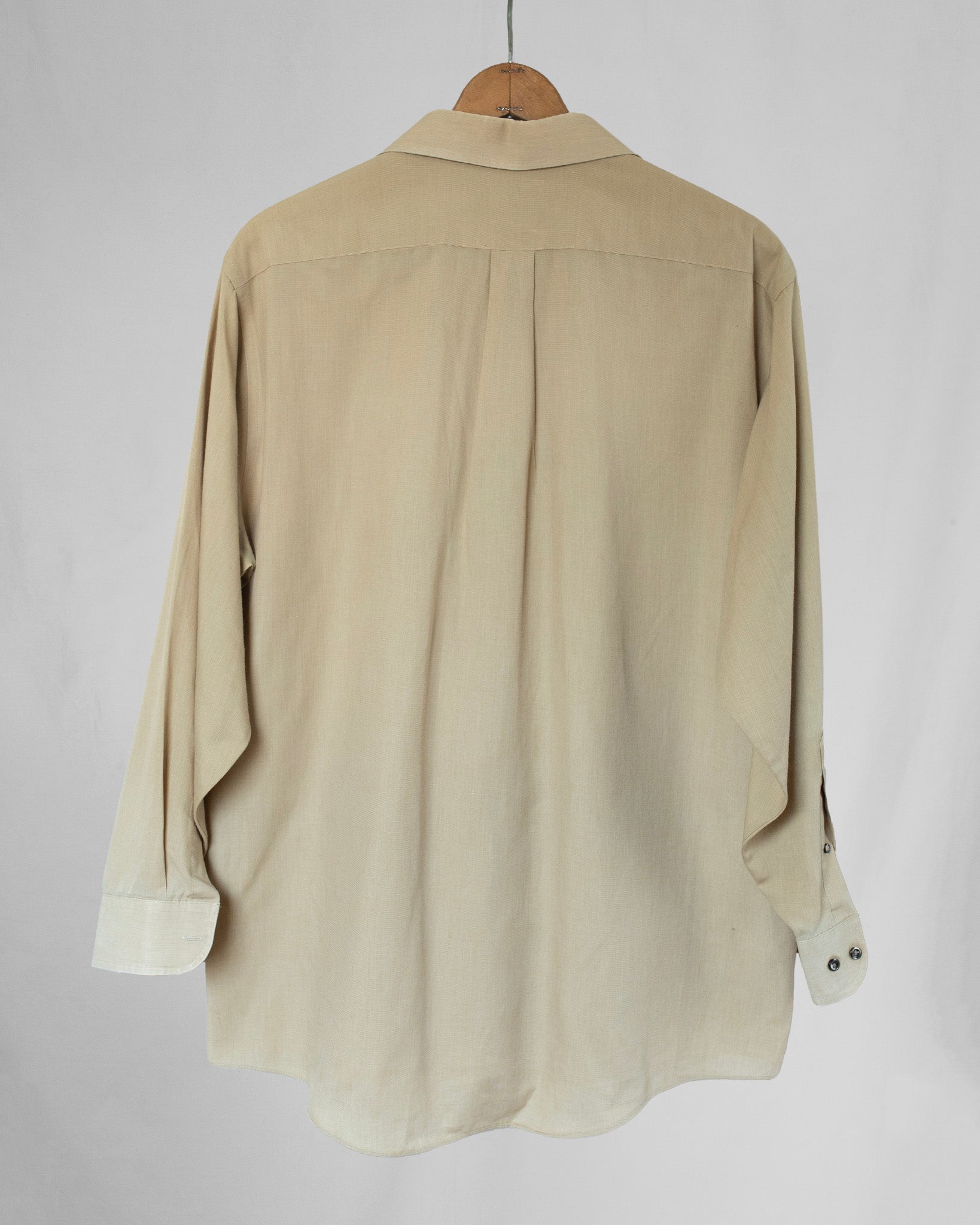 Pale yellow shirt on a wooden hanger against a plain background