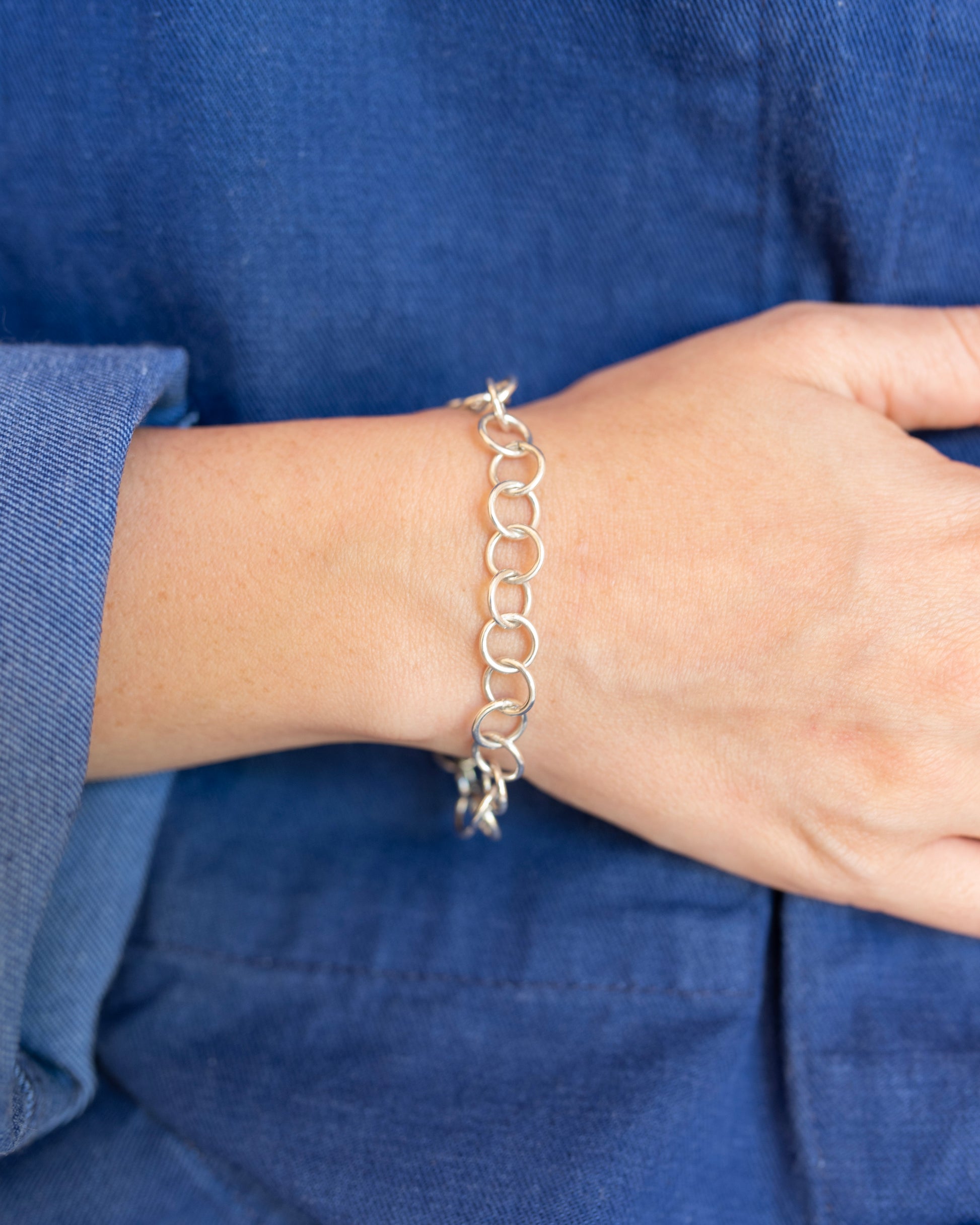 Close up of a hand wearing a silver chain link bracelet thats worn by someone in a blue canvas jacket.