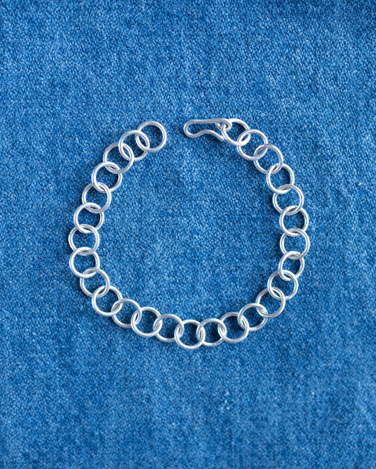 A silver chain link bracelet with a spring-ring design and a lobster clasp, displayed on a textured blue fabric background.