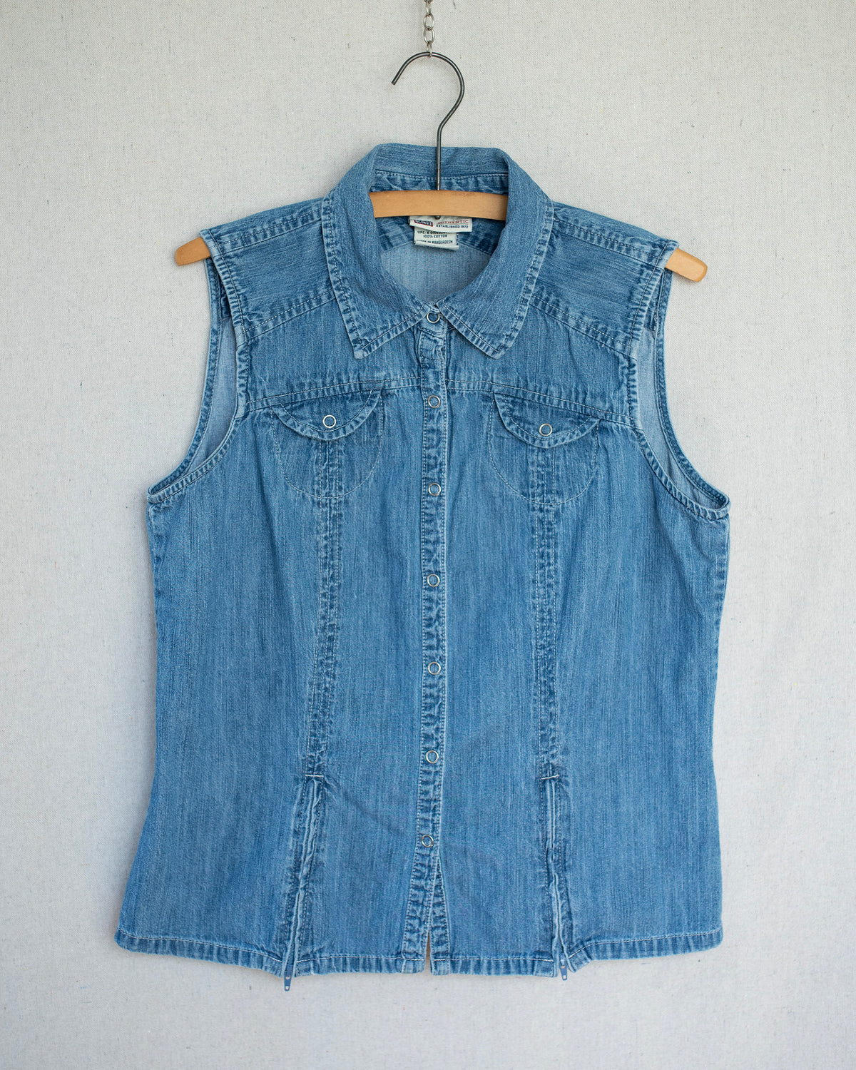 Denim top hanging on a wooden hanger featuring two zippers on the bottom hems