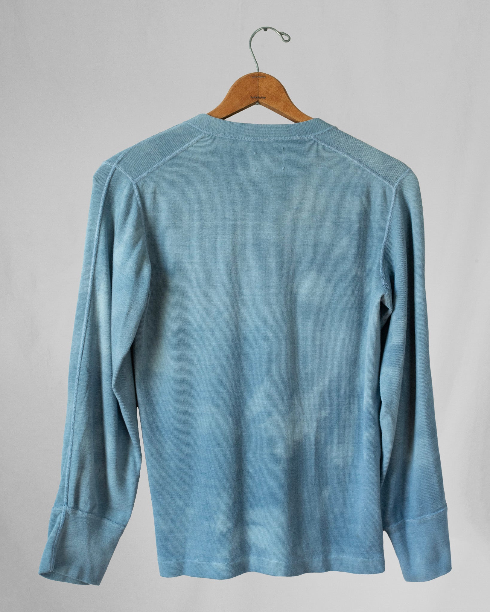 Blue long-sleeve shirt on a hanger against a gray background.