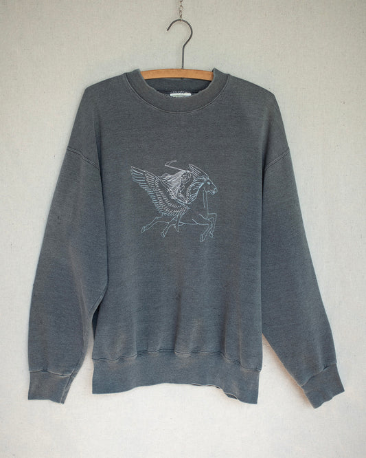Dark grey crewneck sweatshirt with a two tone embroidery on front hanging on a wooden hanger.