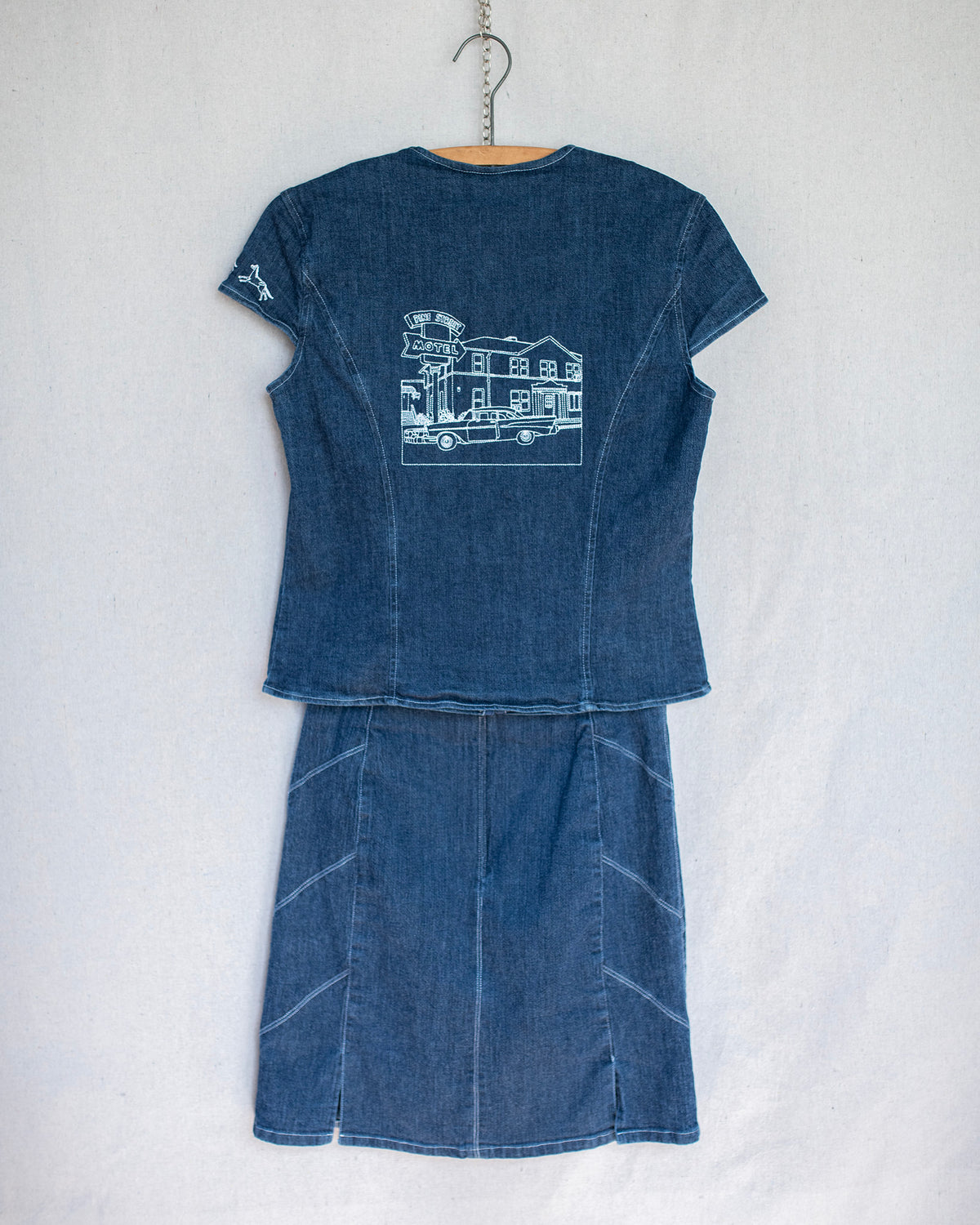 Denim two piece set showing the back of the hanging short sleeve top and skirt that features embroideries throughout.