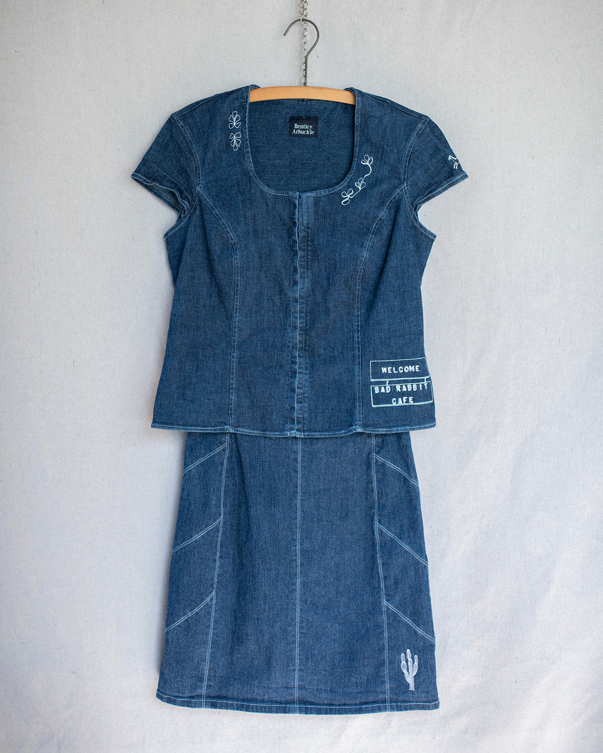 Denim two piece set consisting of a short sleeve top and skirt that are hanging and adorned with multiple embroideries.