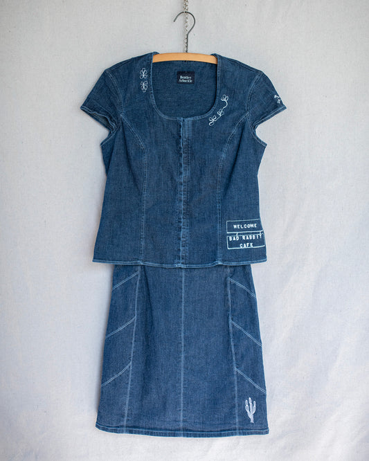 Denim two piece set consisting of a short sleeve top and skirt that are hanging and adorned with multiple embroideries.