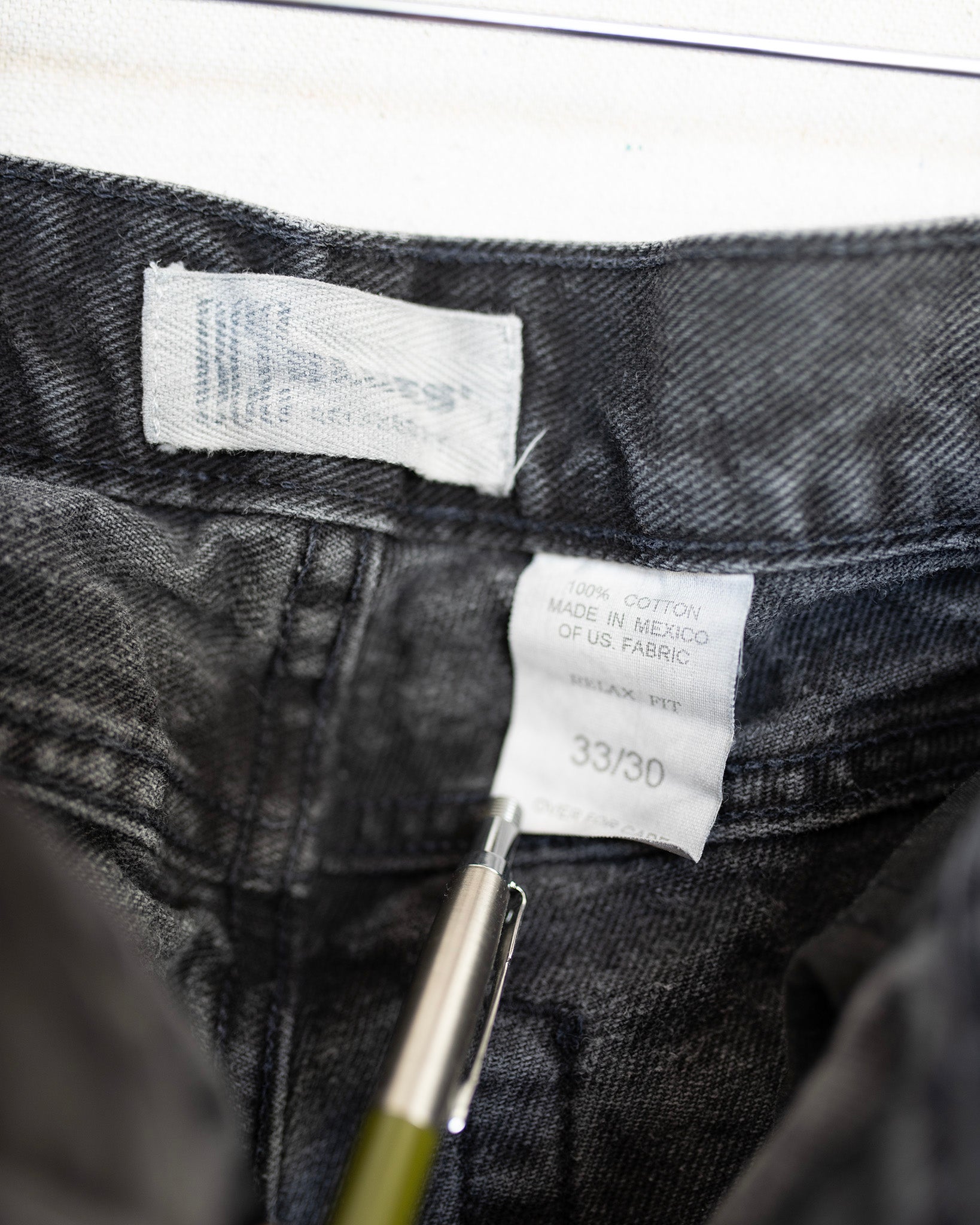 Close-up of a label on black denim jeans with a pen pointing at it.
