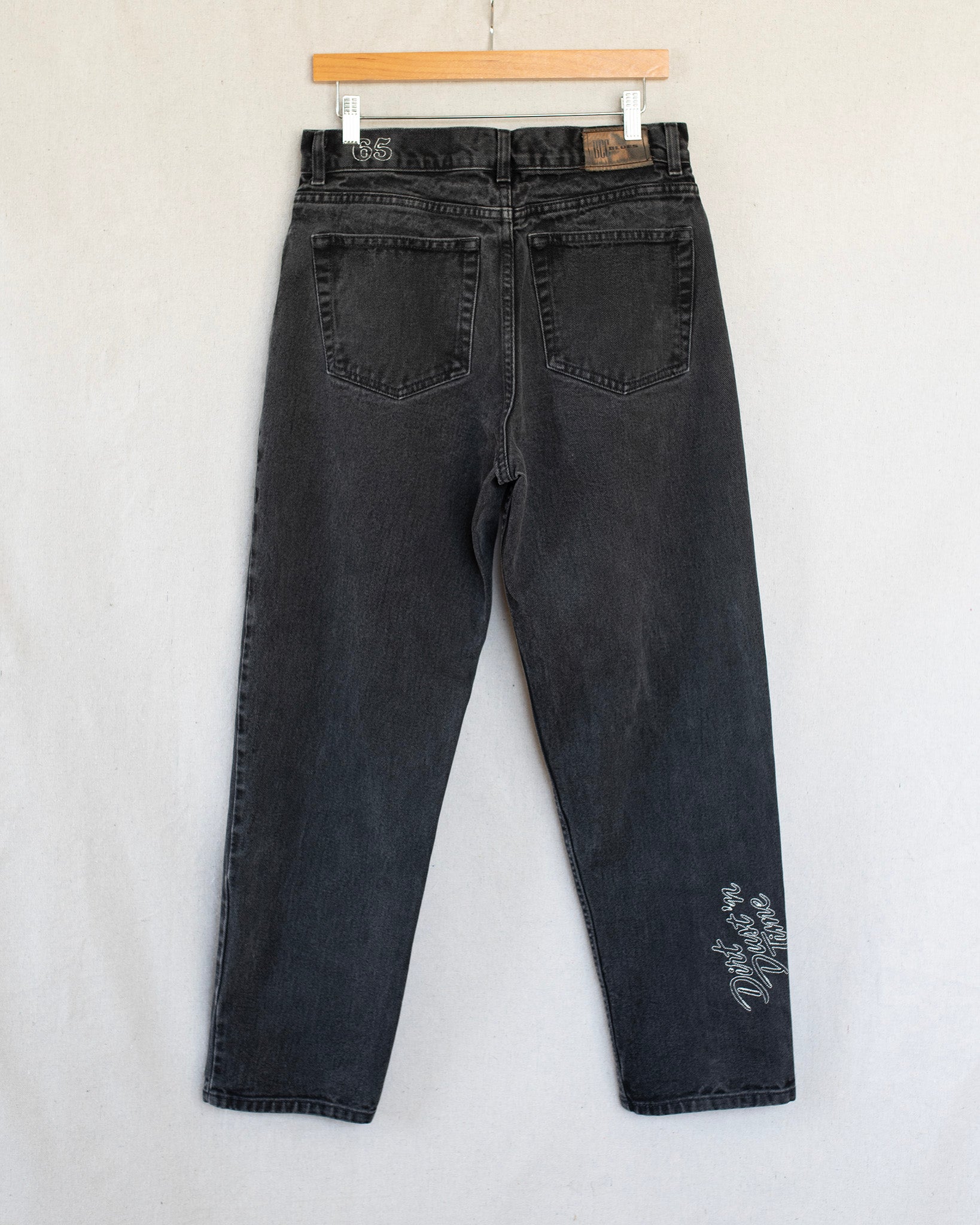 Black jeans hanging on a wooden hanger against a white background