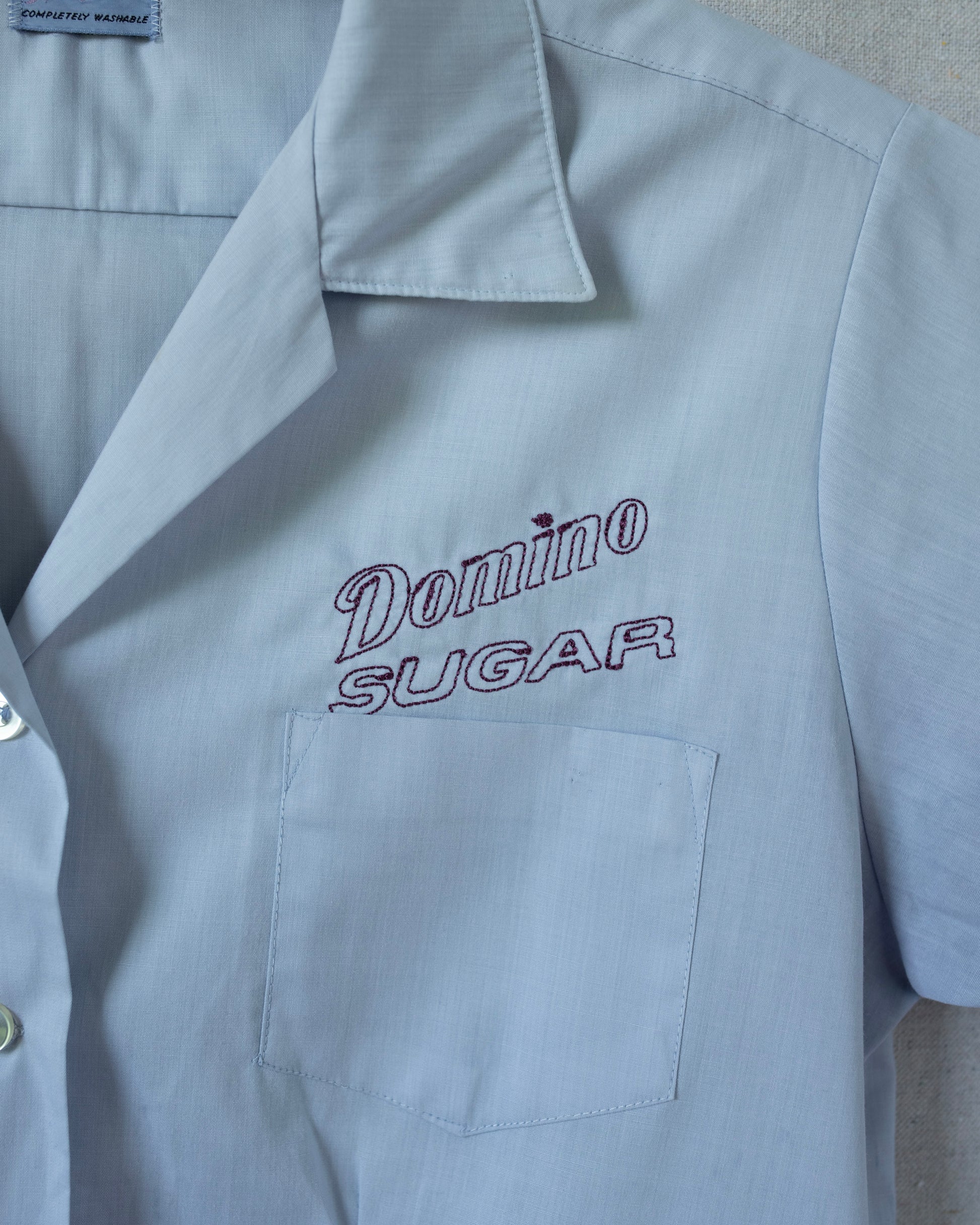Light blue shirt with 'Domino Sugar' embroidery on a gray background