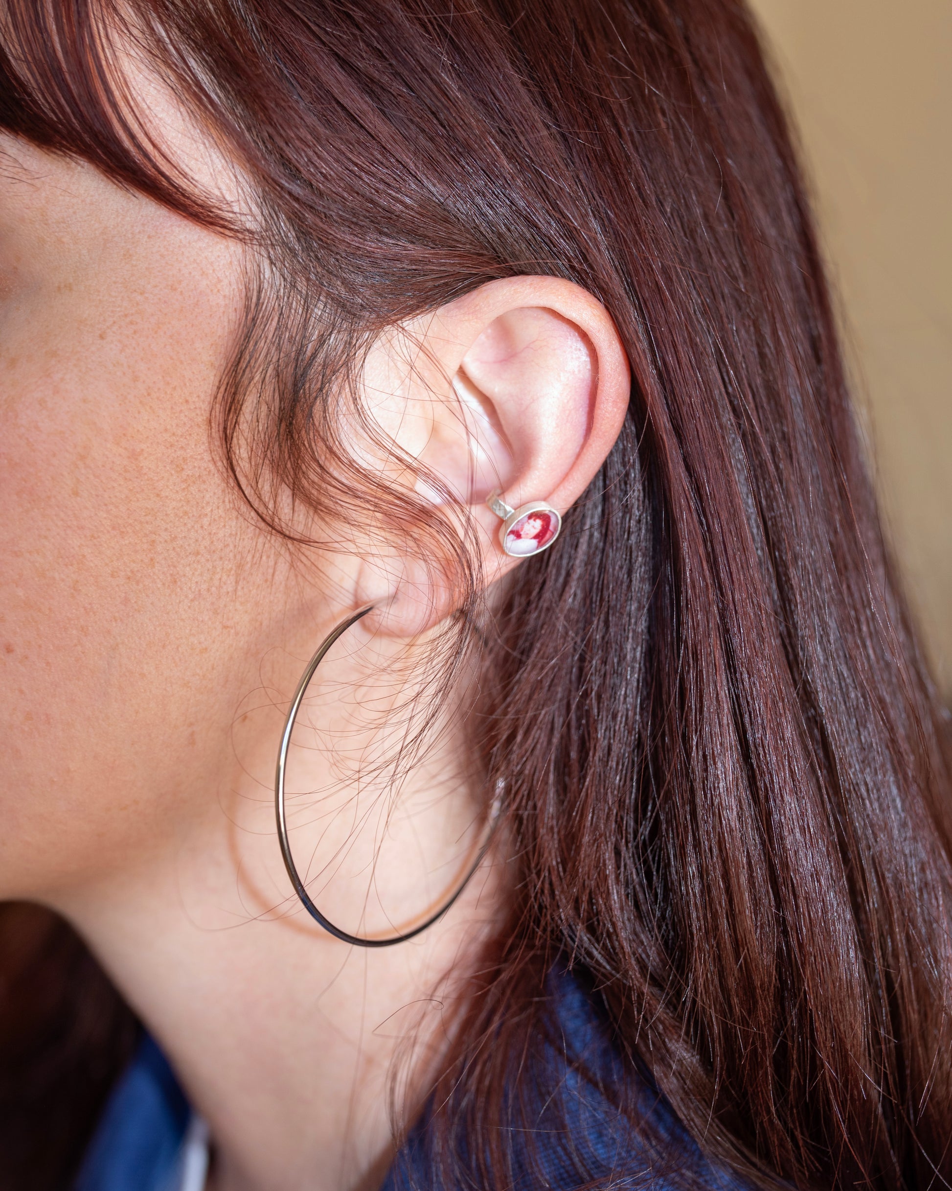 Close up of the side of a woman's face with her hair behind her ear wearing a silver hoop and custom made ear cuff.