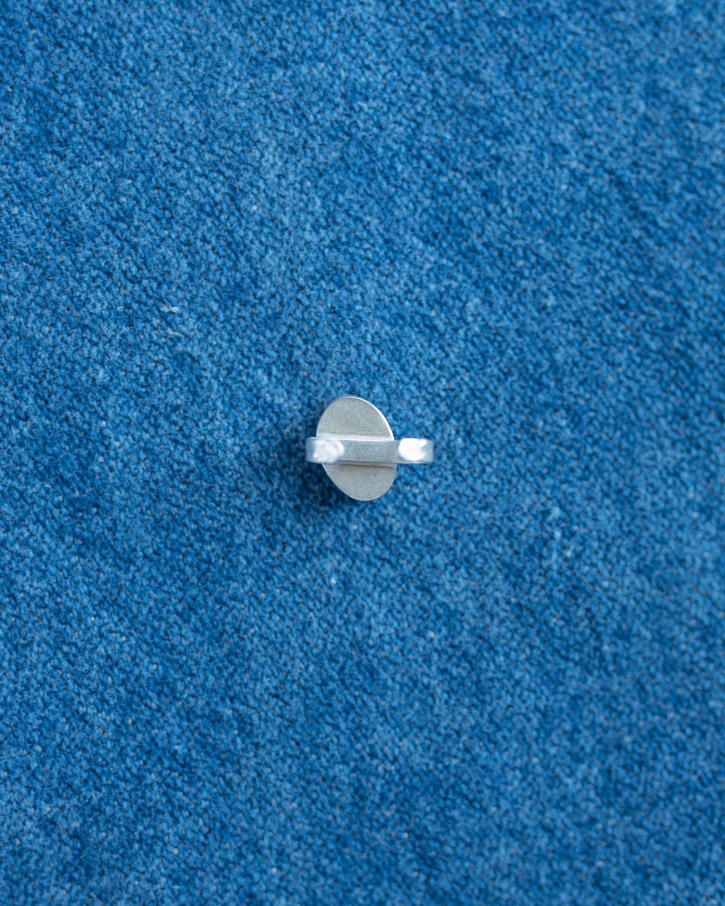 A small silver metal hardware piece,  shown on a textured blue background.