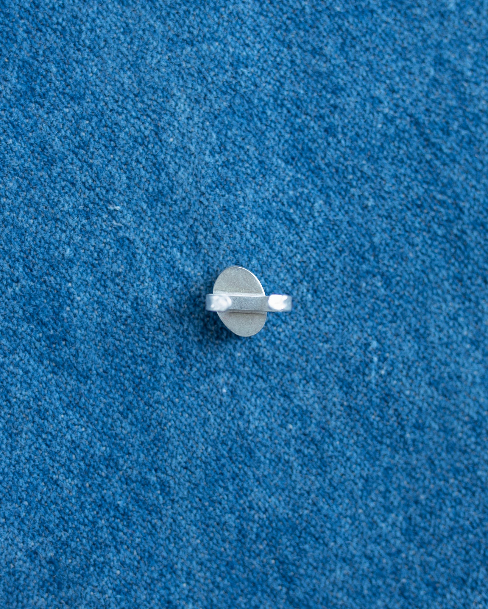 A small silver metal hardware piece,  shown on a textured blue background.