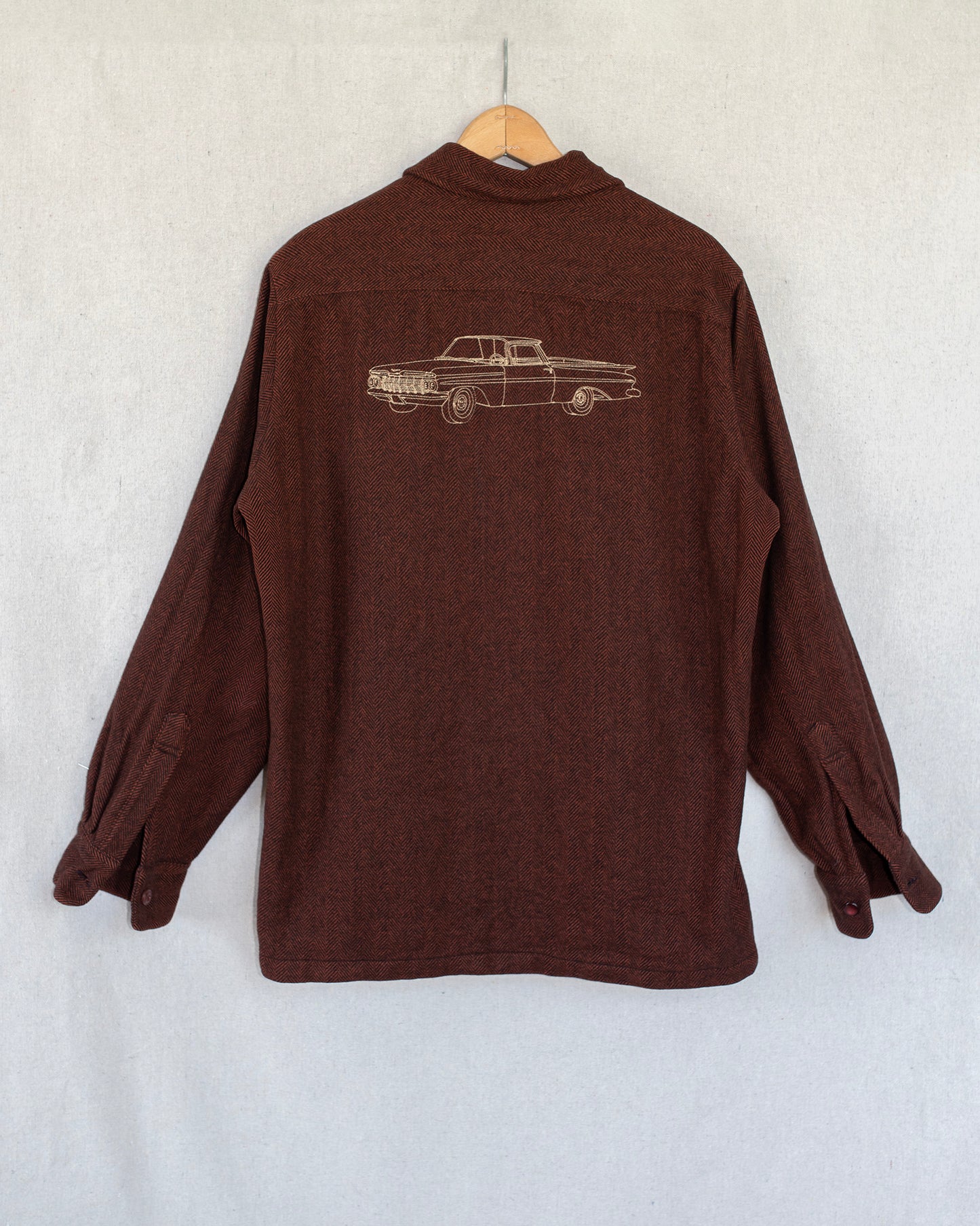 Brown shirt with an embroidery on the back, hanging against a white wall.