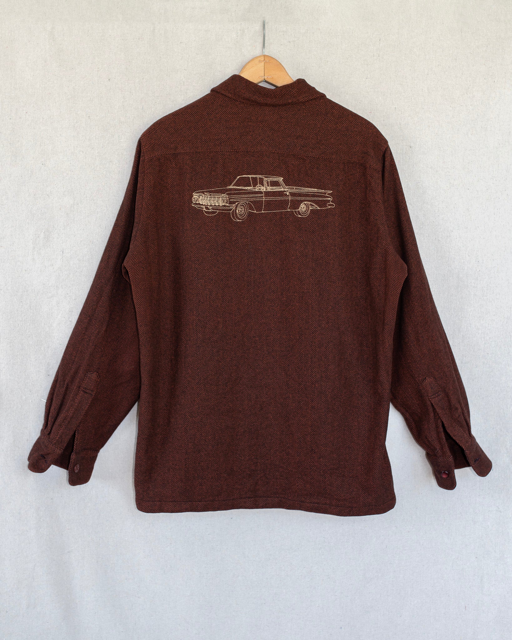 Brown shirt with an embroidery on the back, hanging against a white wall.