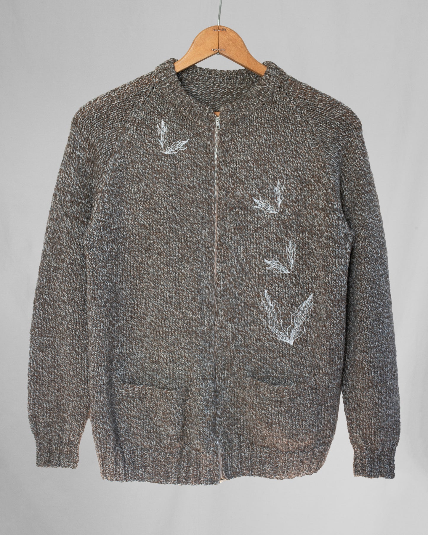 Brown sweater with white designs on a hanger against a gray background