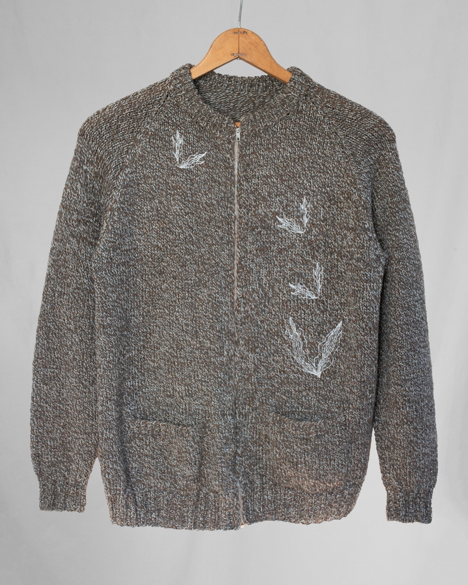 Brown sweater with white designs on a hanger against a gray background