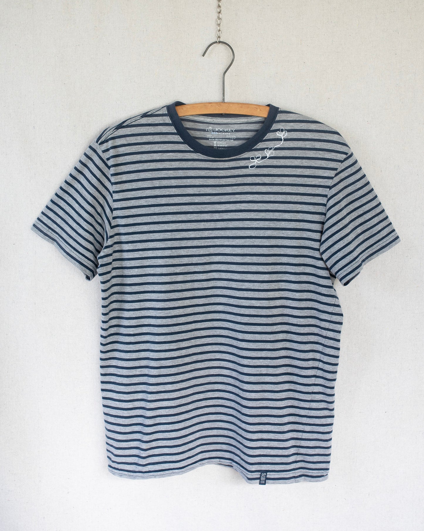 Striped t-shirt with a floral embroidery under the collar on a hanger against a white background