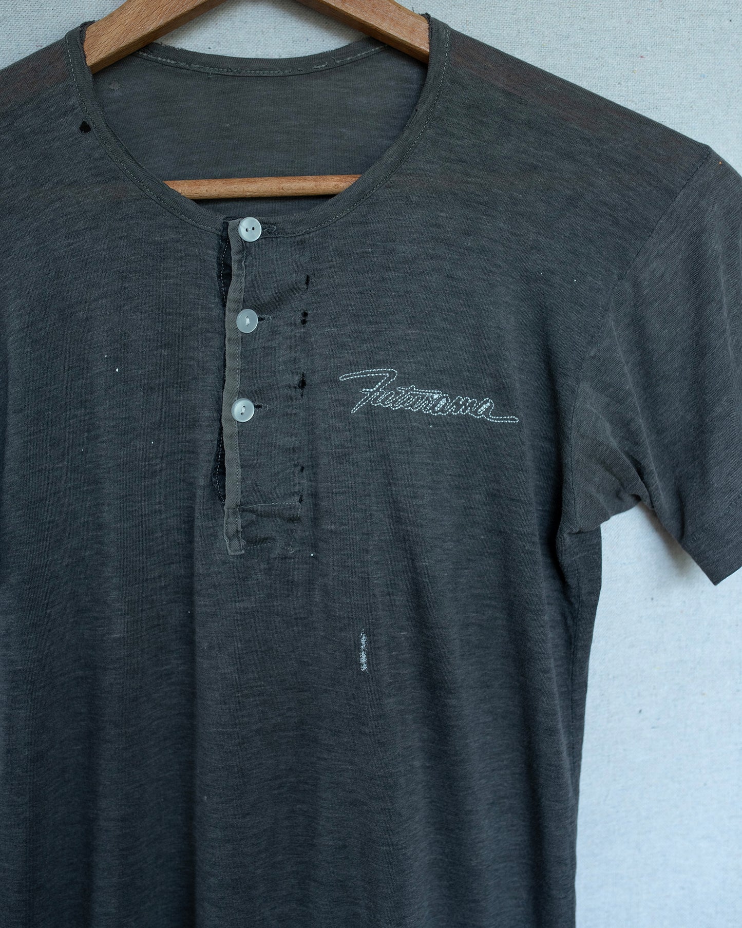 Dark gray shirt with embroidery on a wooden hanger against a light background