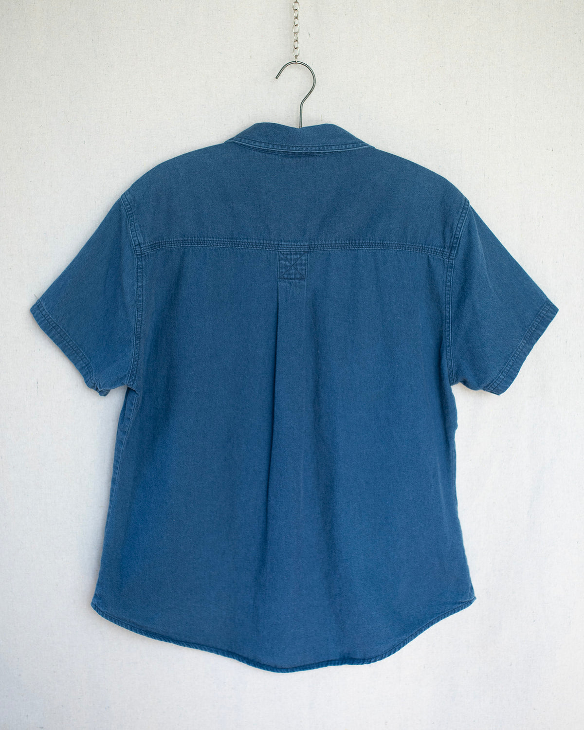 Denim short sleeve hanging on a wooden hanger.