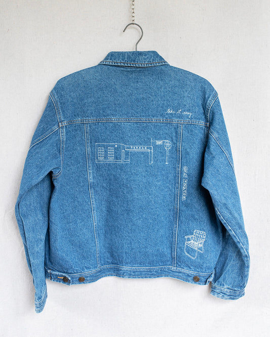 Blue denim jacket with embroidered designs on a white background
