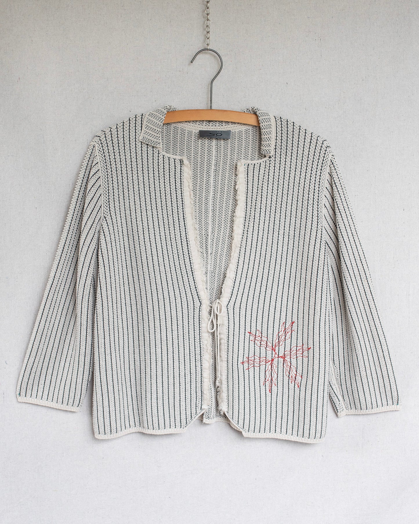 Striped cardigan with a floral design on a hanger against a white background