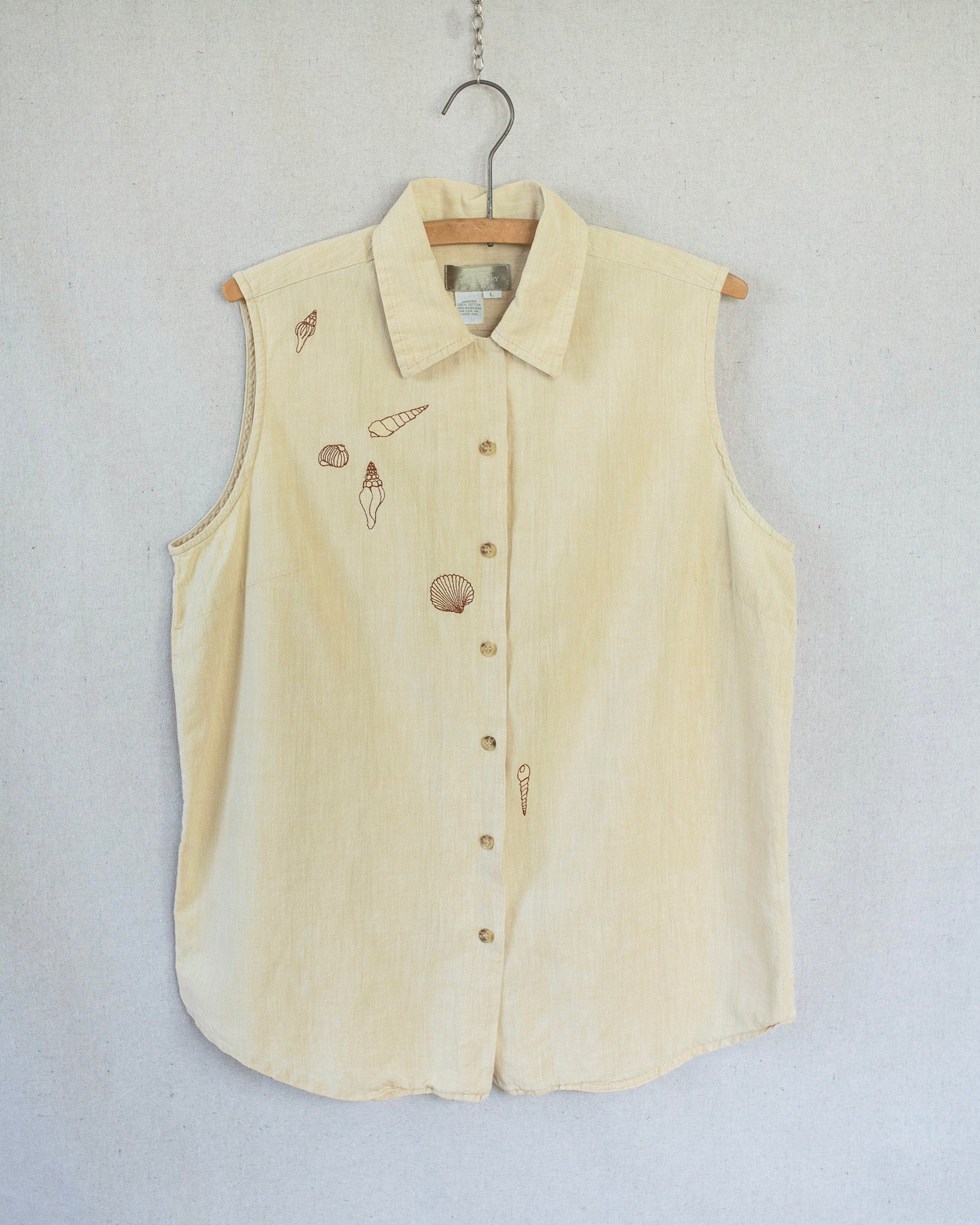 Yellow sleeveless button-up shirt with embroidered seashell designs on a white background