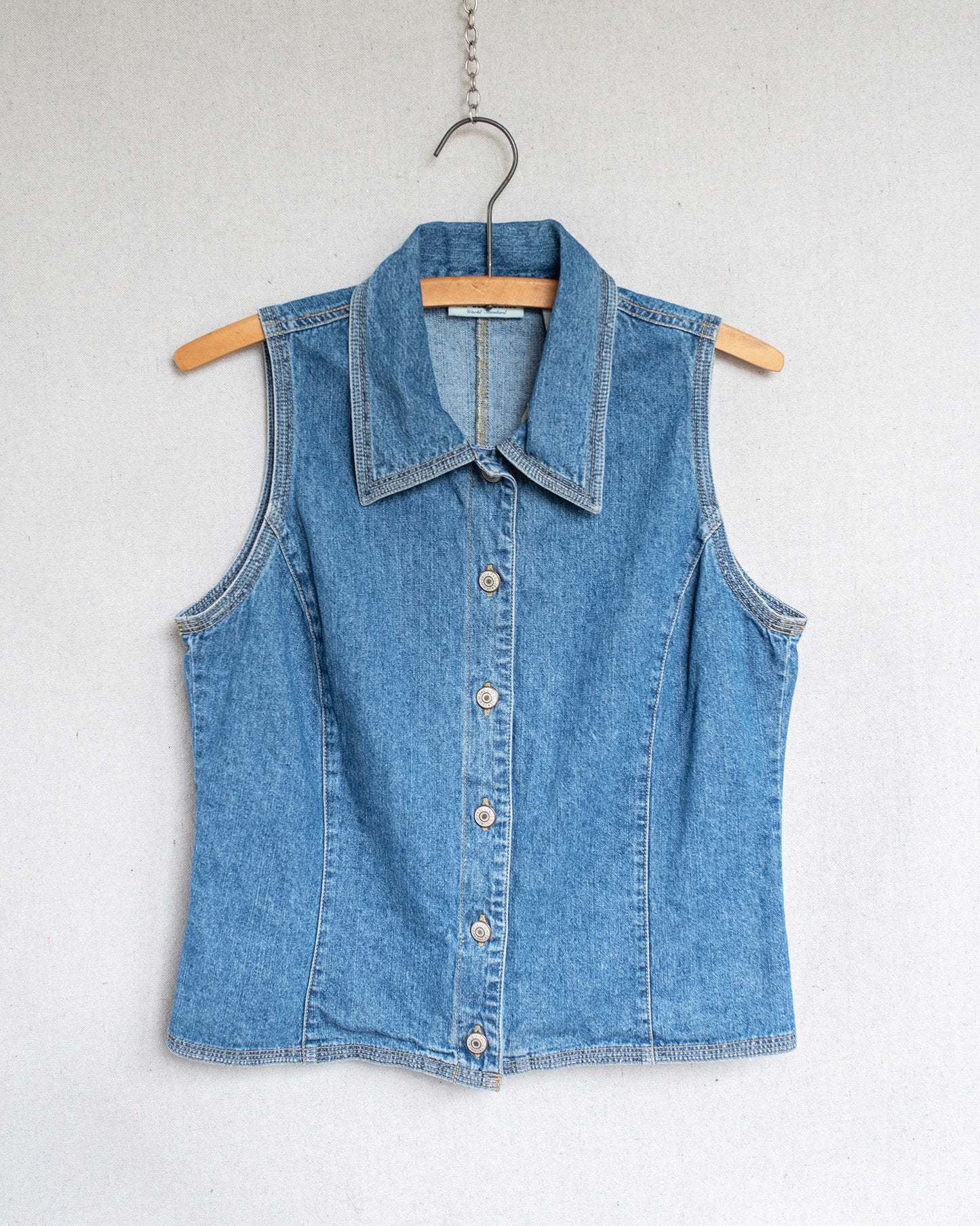 Blue denim vest on a hanger against a white background