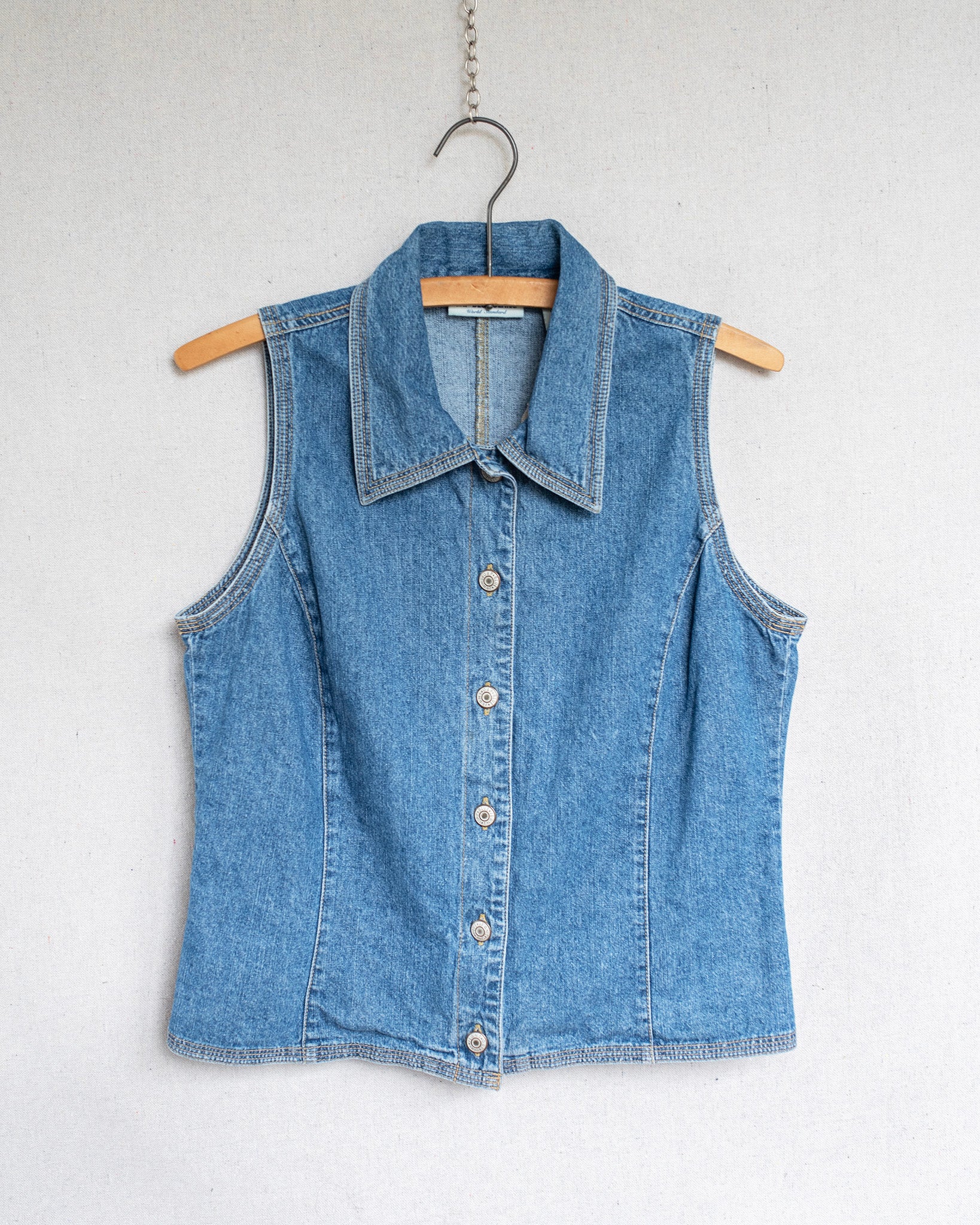 Blue denim vest on a hanger against a white background