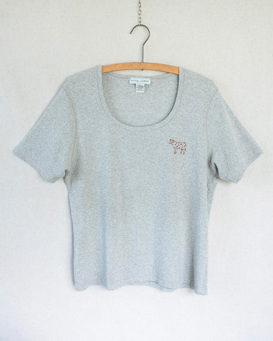Grey t-shirt with a small cow embroidery hanging against a white background