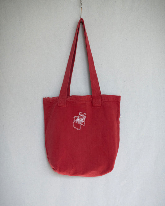Hanging red canvas tote bag that has a small lawn chair embroidery on top center.