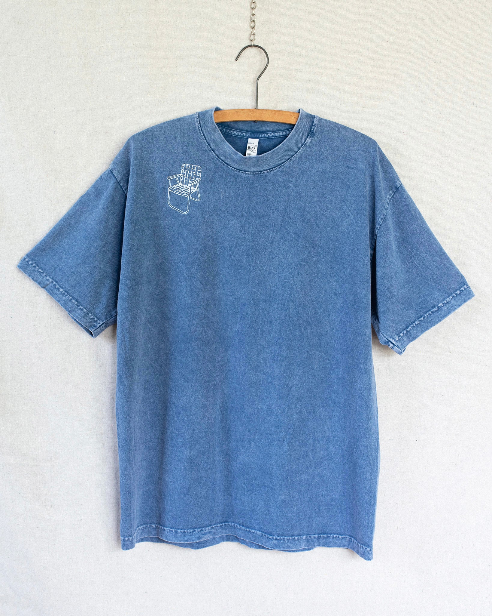 Blue t-shirt with a lawn chair embroidery on a hanger against a white background