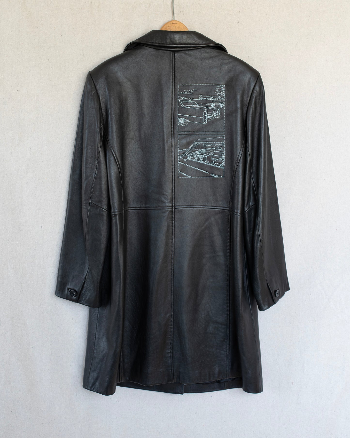 Black leather coat with embroideries on the back, hanging against a white background