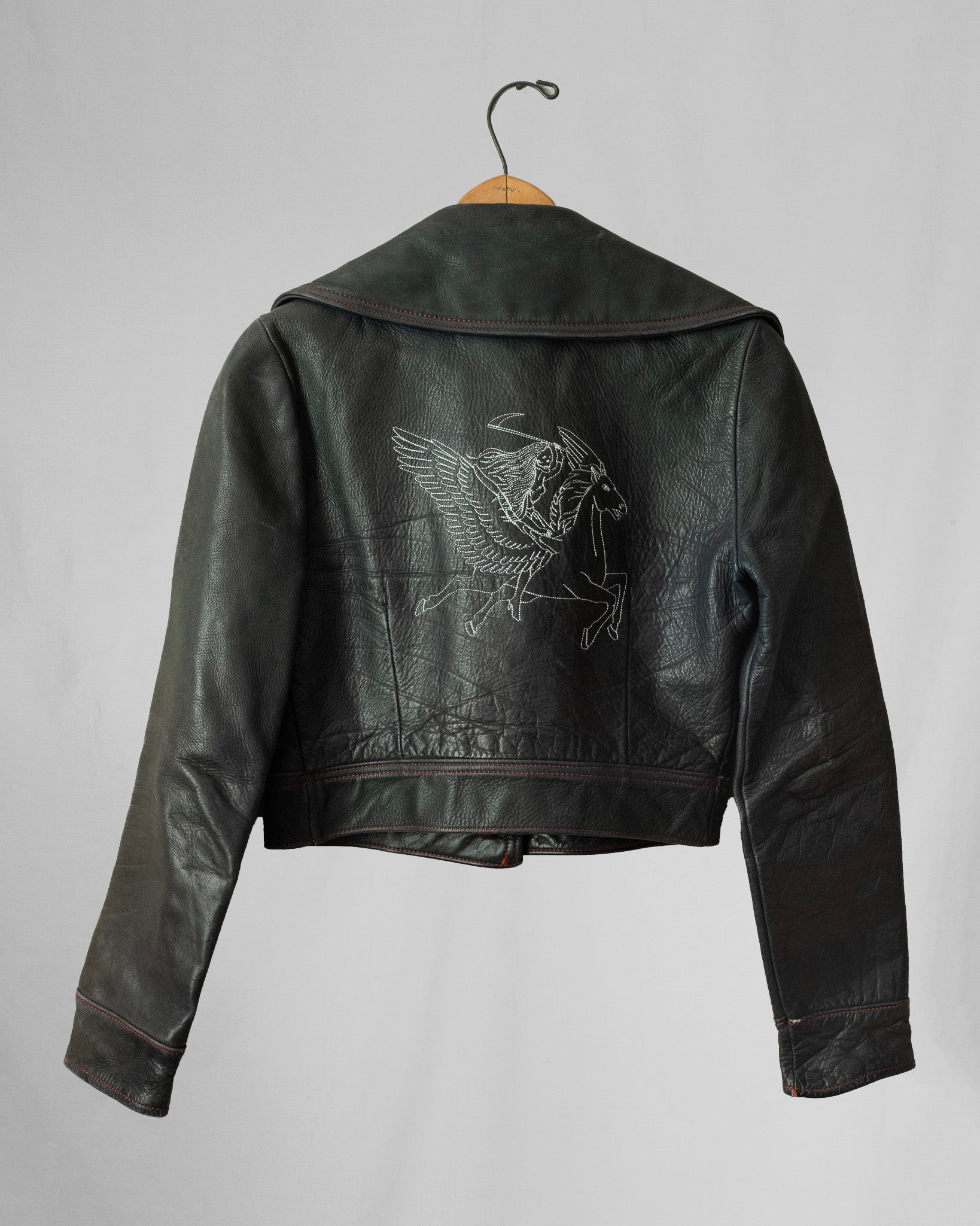 Black leather jacket with embroidery on a hanger against a gray background