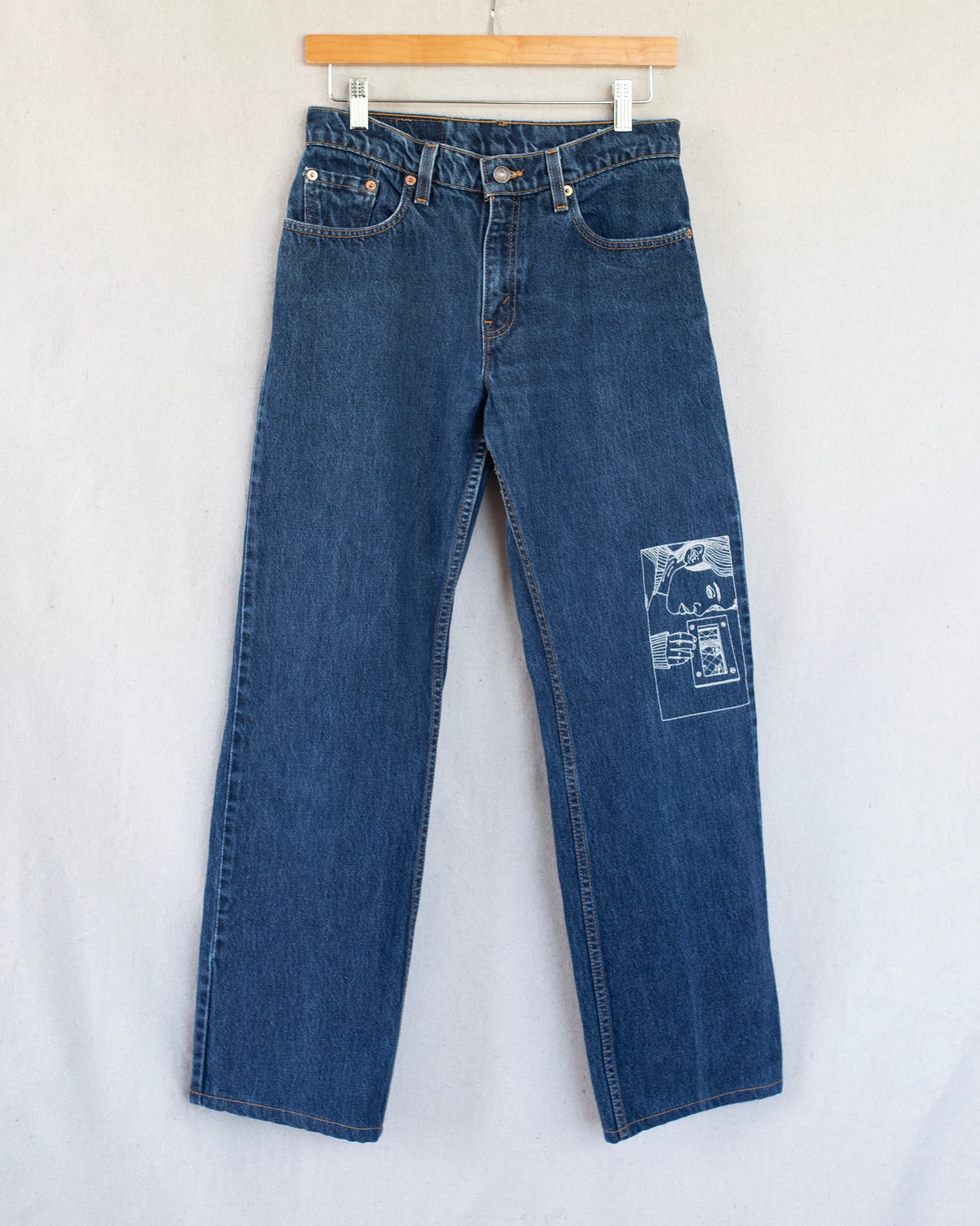 Blue jeans with an embroidery on one leg on a white background