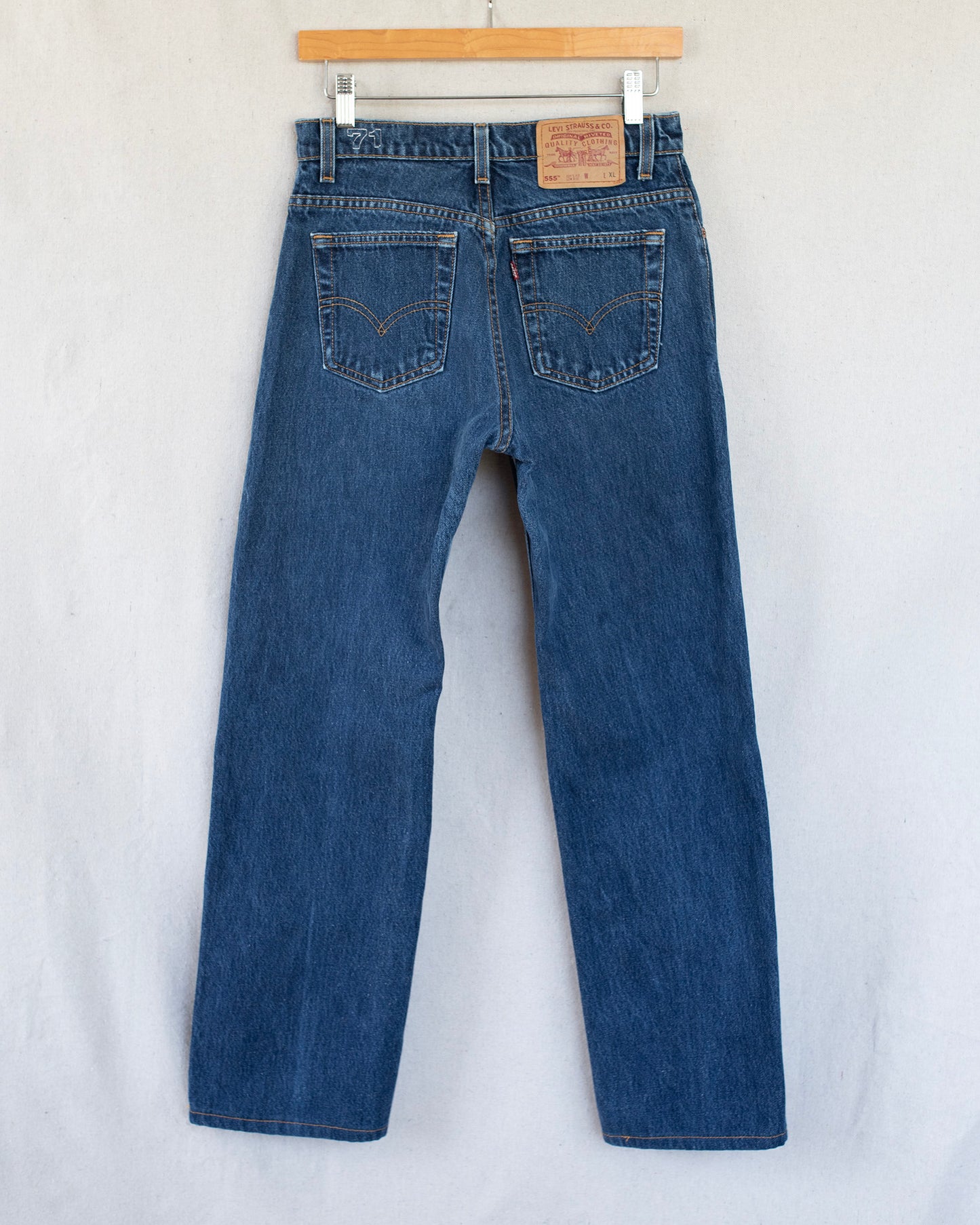 Blue jeans hanging on a wooden hanger against a white background