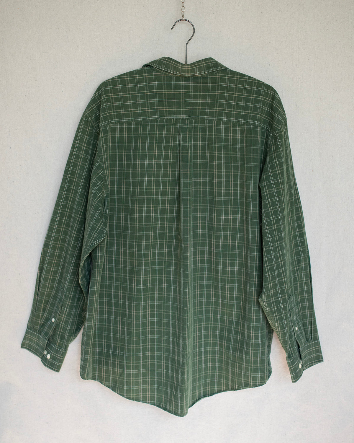 A green long sleeve plaid shirt hanging against a canvas background.