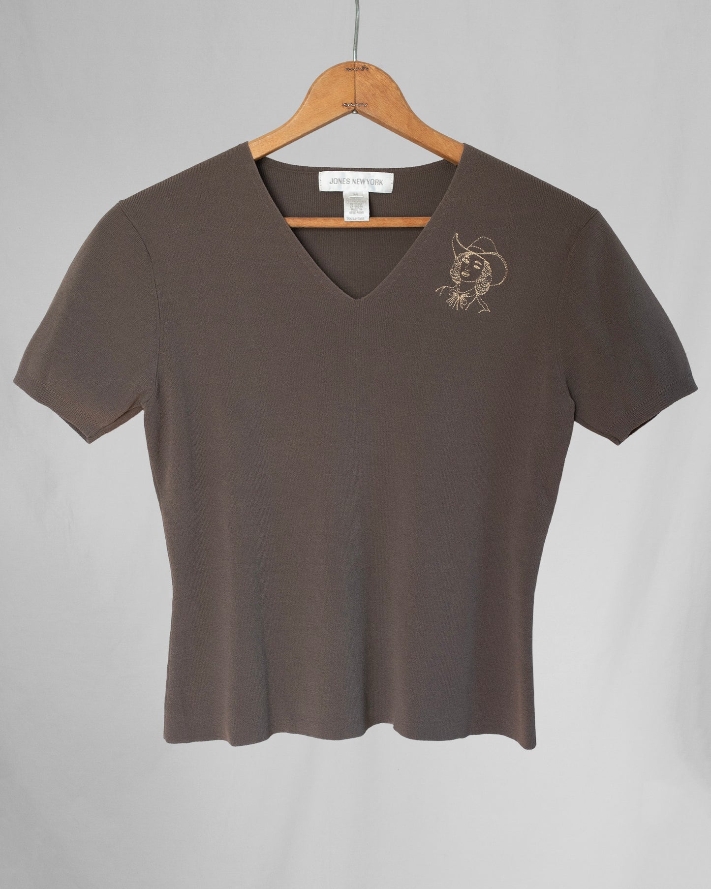 Brown t-shirt with a small design on a hanger against a gray background