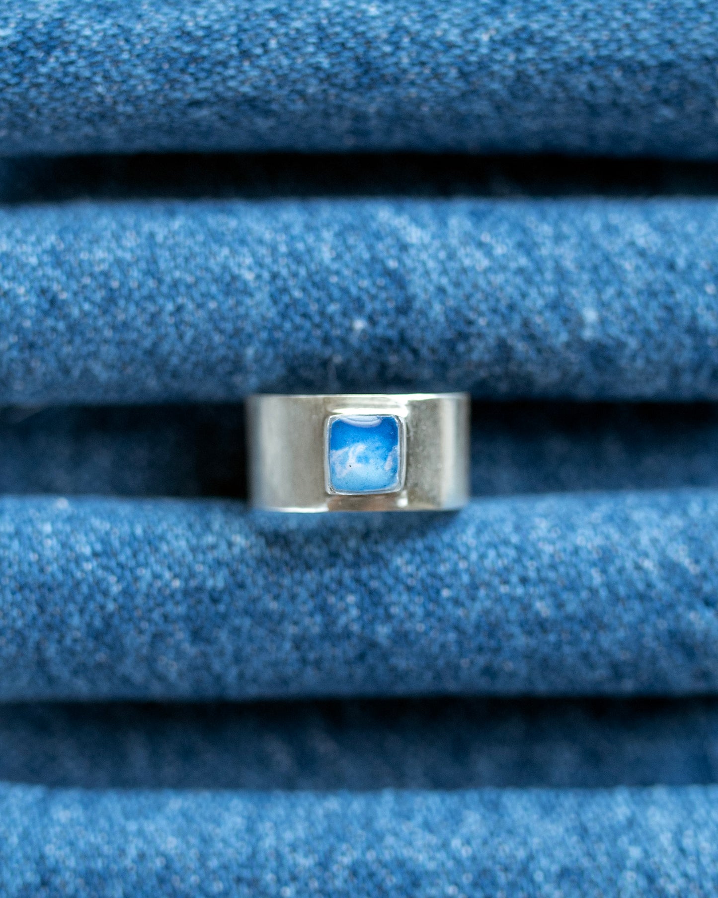 Thick silver ring with a bezel and mountain motif ontop of a denim ring stand.