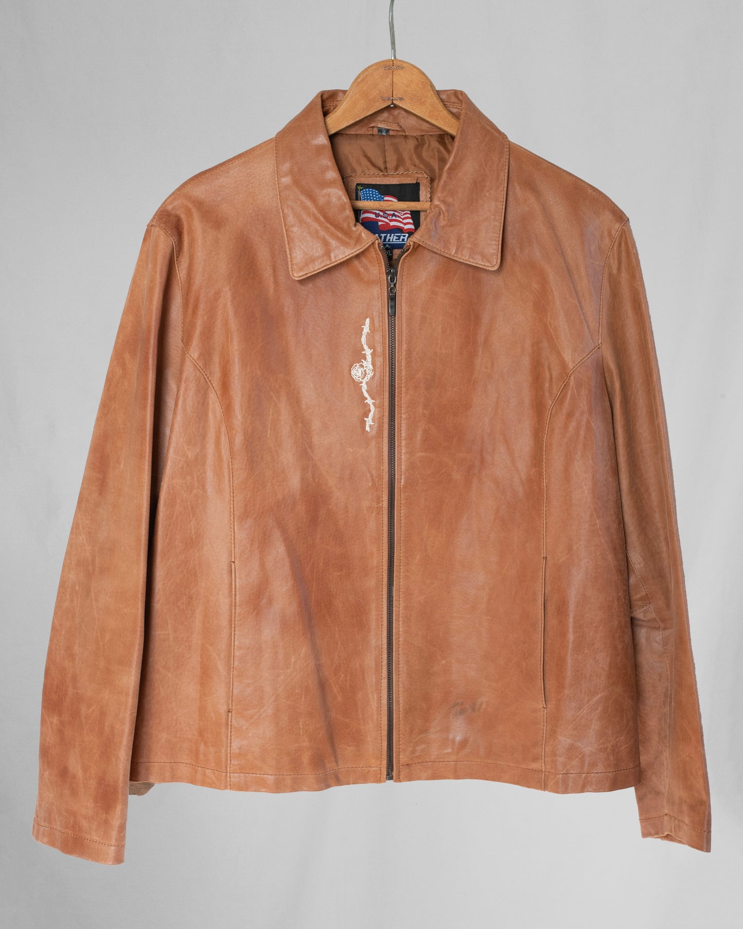 Brown leather jacket on a hanger against a gray background