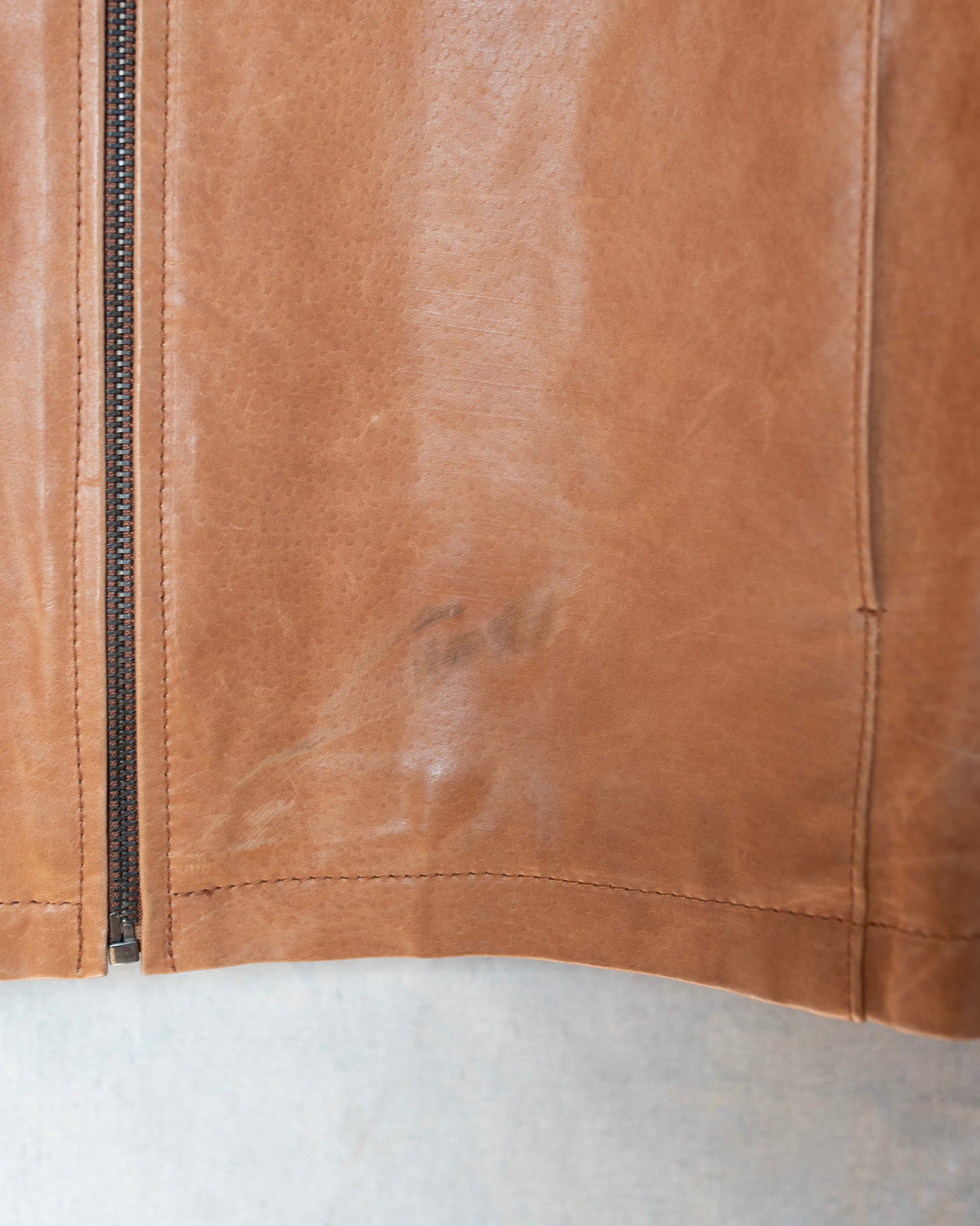 Close-up of a brown leather jacket with visible wear on a white background