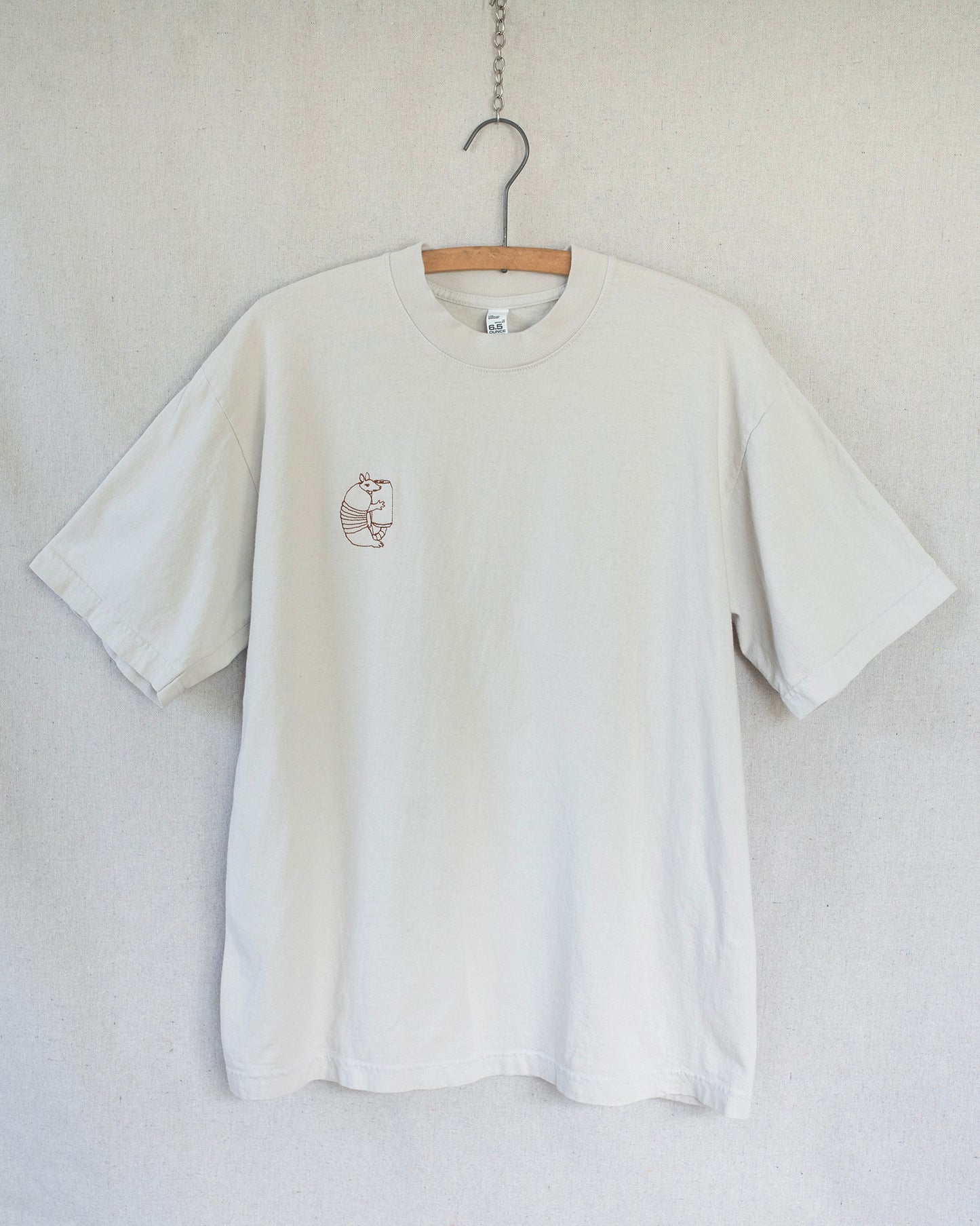 Off white t-shirt with a lawn chair embroidery on a hanger against a light gray background