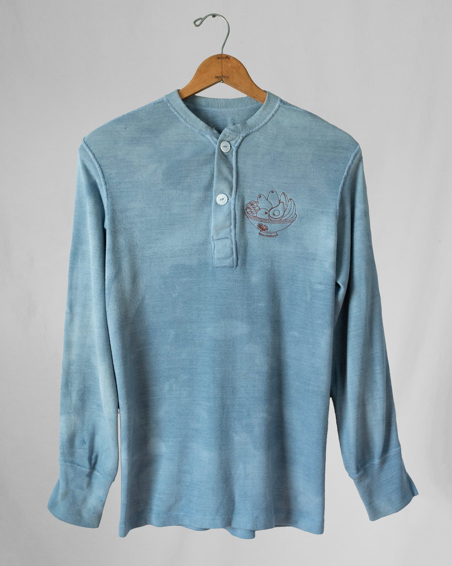 Blue long-sleeve shirt with an embroidery on a hanger against a gray background
