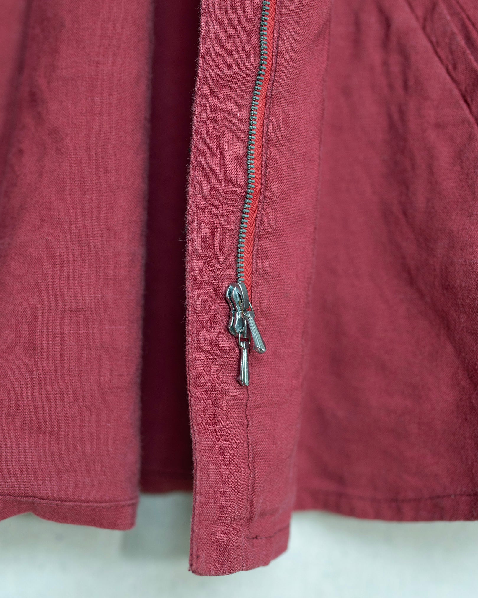 Close-up of a dusty red red fabric garment featuring a double silver zipper with a decorative pull tab.
