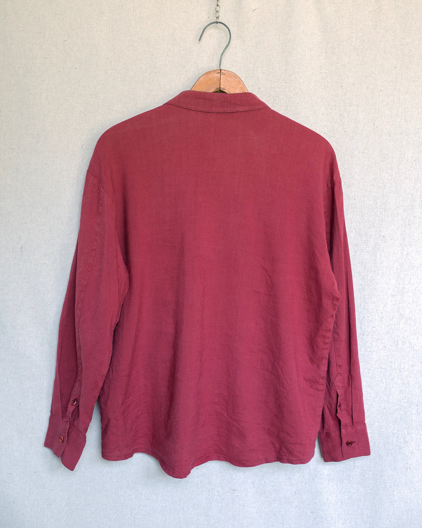 A dusty red jacket hanging on a wooden hanger against a light gray textured wall.