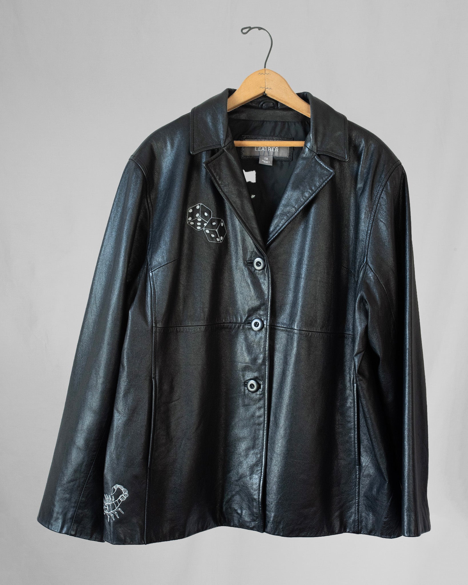 Black leather jacket with embroidery on a hanger against a gray background