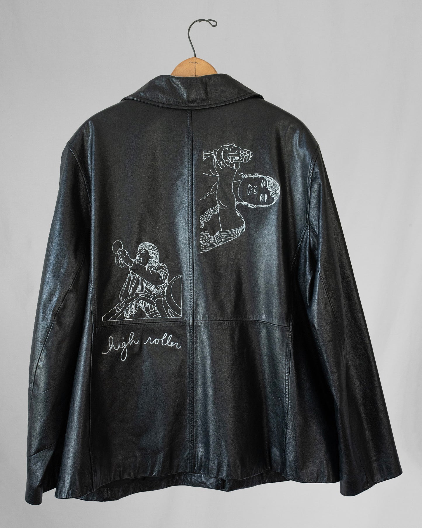 Black leather jacket with embroidered designs on a gray background