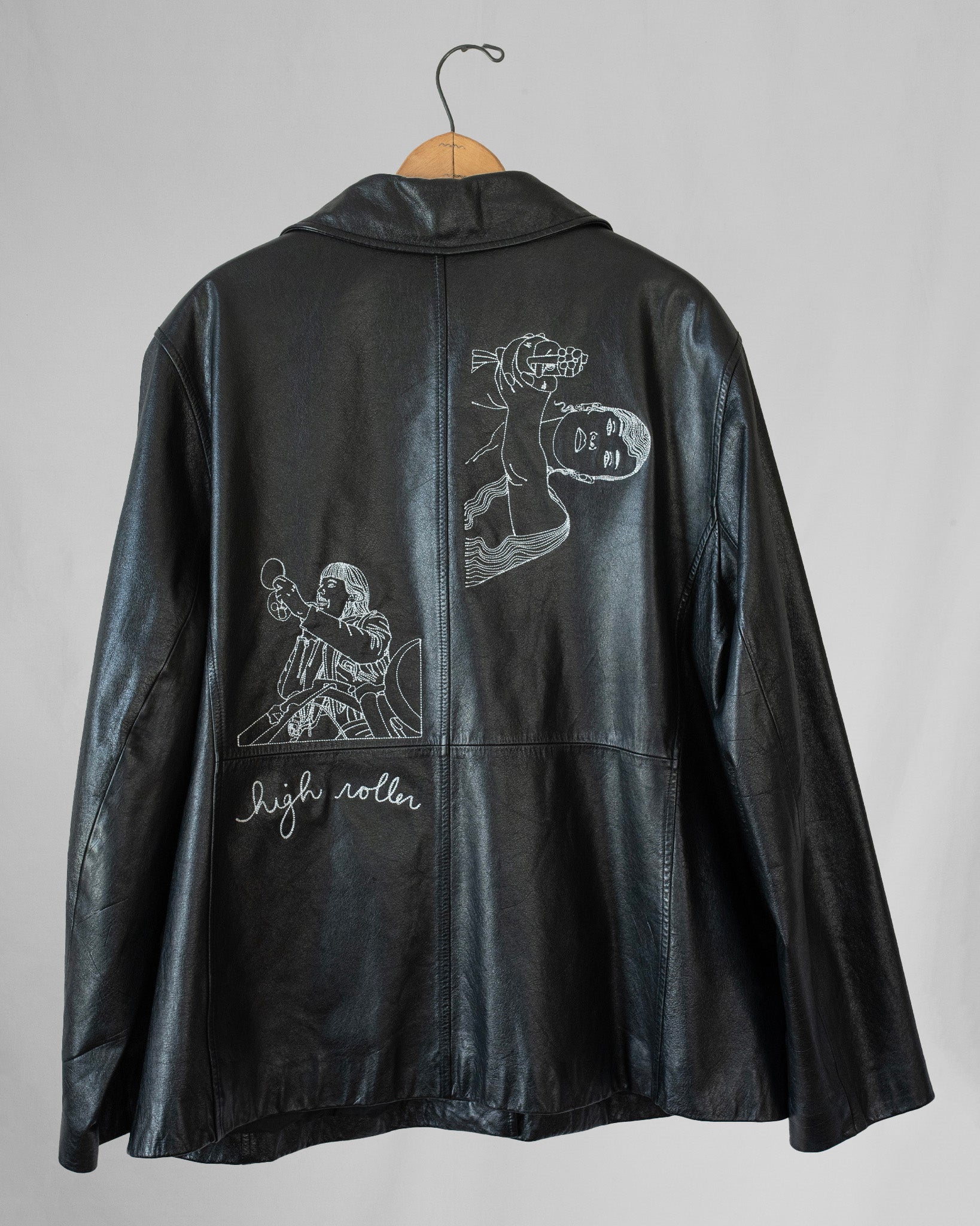 Black leather jacket with embroidered designs on a gray background